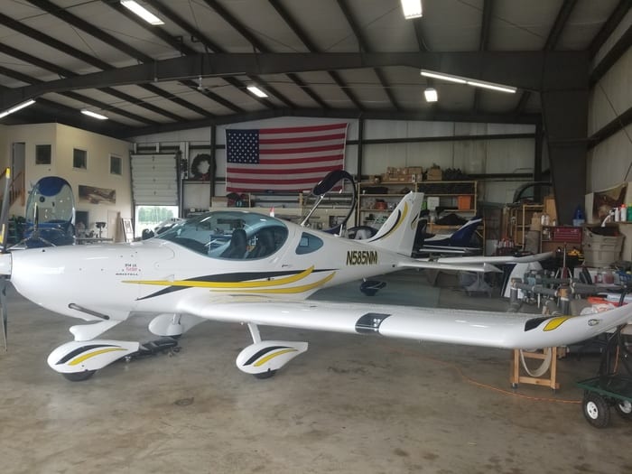 A small airplane in an aircraft hangar with a flag on the wall.