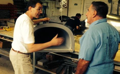 Two men standing in front of a pizza oven.